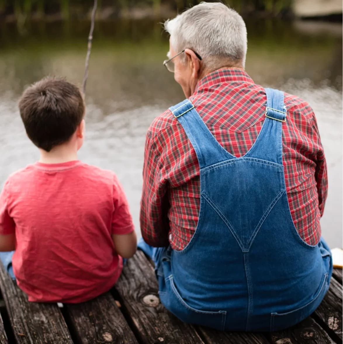 A grandfather and his grandson sitting together on a dock, fishing